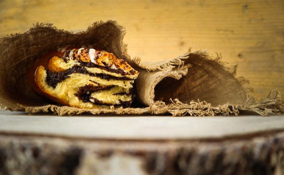 Fresh poppy seed roll on natural linen napkin on rustic wooden background