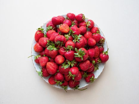 Fresh red strawberries on a white ceramic plate, on a light grey background, top view