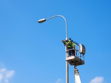 Two workers repairing the street lighting support