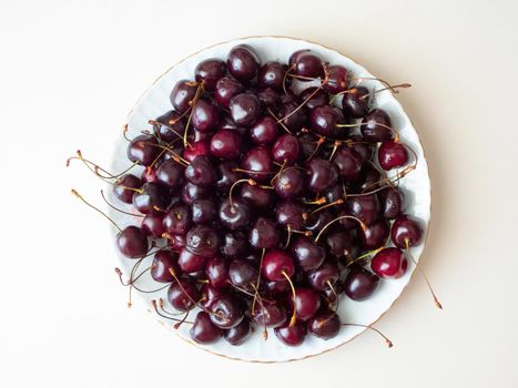 Fresh cherries on a white ceramic plate, on a light grey background, top view