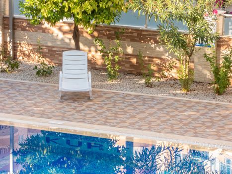 Alanya, Turkey - August 24, 2020: White plastic sun lounger nearby the pool on a summer morning