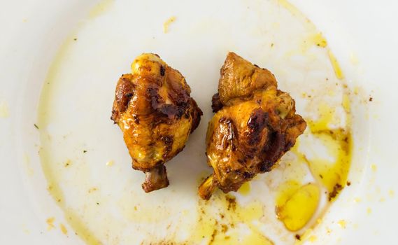 Chicken drumsticks on a white plate with oil around.