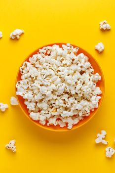 Popcorn in an orange bowl on yellow background. Vertical image. Top view.