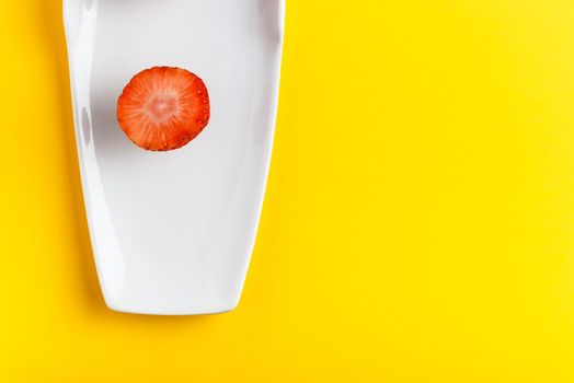 Slice of fresh strawberry in a white dish on yellow background. Horizontal image seen from above.