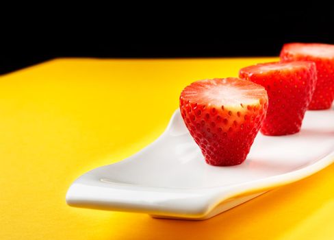 Fresh strawberries in a white plate on yellow background. Horizontal image