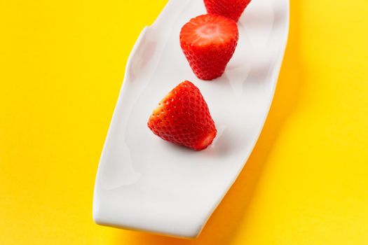 Fresh strawberries in a white dish on yellow background. Horizontal image.