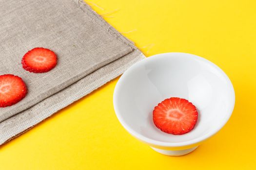 Three slices of fresh strawberries in a round white plate on yellow background and sackcloth. Horizontal image.