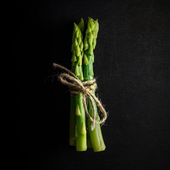 Asparagus. Bunch of fresh green asparagus tied on black background. Healthy vegetarian food. Square image