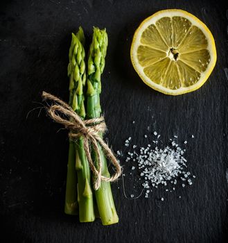 Asparagus. Bunch of fresh green asparagus with coarse salt and a slice of lemon on a slate plate. Healthy vegetarian food. Square image