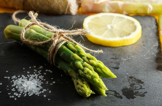 Asparagus. Bunch of fresh green asparagus close-up with coarse salt and a slice of lemon on a slate plate. Healthy vegetarian food. Horizontal image.