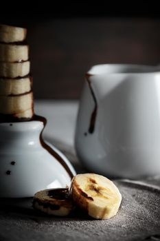 Delicious dessert of fresh banana slices with chocolate on top on a sackcloth seen from close up. Vertical image of dark moody style.