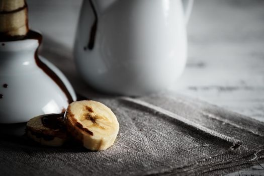 Delicious dessert of fresh banana slices with chocolate on top on a sackcloth seen from close up. Horizontal image of dark moody style.