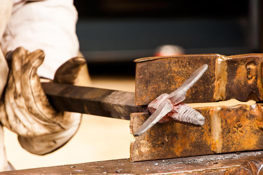 Blacksmith working a metal piece with the hammer on a craftsmen's market.