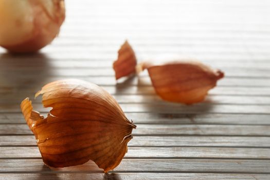 Onion skin in the foreground against the light with more onion skins in the background on wooden boards. Horizontal image.