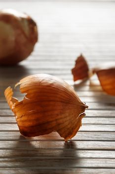 Onion skin in the foreground against the light with more onion skins in the background on wooden boards. Vertical image.