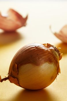 Onion with backlight with onion skins at the bottom on yellow surface. Healthy life concept. Vertical image.