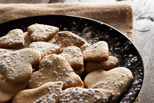 Delicious home-made heart-shaped cookies sprinkled with icing sugar on sackcloth and wooden boards. Horizontal image seen against backlight.