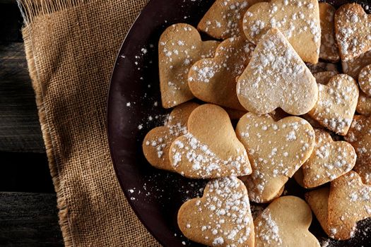 Delicious Home-made heart-shaped cookies sprinkled with icing sugar on sackcloth and wooden boards. Horizontal image seen from above.