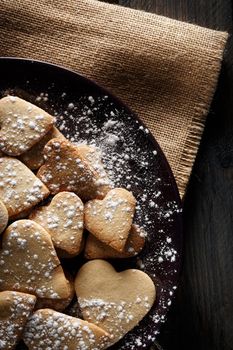 Delicious home-made heart-shaped cookies sprinkled with icing sugar on sackcloth and wooden boards. Vertical image seen from above.