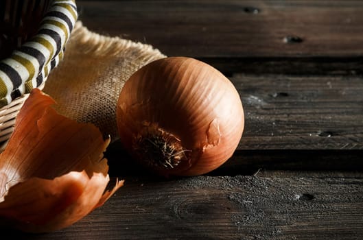 Onion seen close up with wicker basket and sackcloth on wooden boards. Rustic style. Horizontal image.