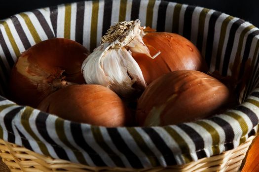 Onions and head of garlic in a wicker basket seen from up close. Rustic style. Horizontal image.