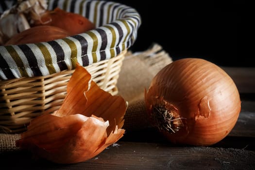 Still life of onions with wicker basket on wooden boards on black background. Rustic style. Horizontal image.