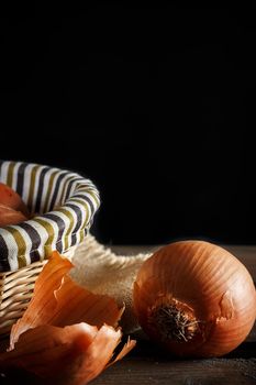 Still life of onions with wicker basket on wooden boards on black background. Rustic style. Vertical image.