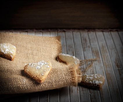 Delicious home-made heart-shaped cookies sprinkled with icing sugar on sackcloth and wooden boards. Horizontal image.