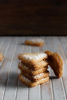 Delicious home-made heart-shaped cookies sprinkled with icing sugar in a wooden board. Vertical image Dark moody style.