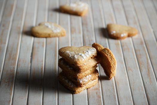 Delicious home-made heart-shaped cookies sprinkled with icing sugar in a wooden board. Horizontal image. Dark moody style.