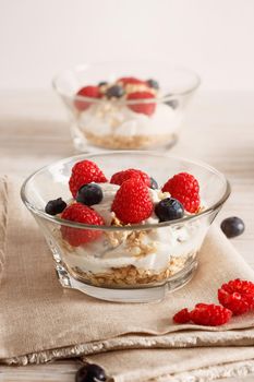 Raspberries, blueberries, cereals and yogurt in a glass bowl on sackcloth and wooden slats. Healthy breakfast for a healthy life. Vertical image.