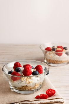 Raspberries, blueberries, cereals and yogurt in a glass bowl on sackcloth and wooden slats. Healthy breakfast for a healthy life. Vertical image.