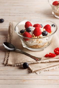 Raspberries, blueberries, cereals and yogurt in a glass bowl on sackcloth and wooden slats. Healthy breakfast for a healthy life. Vertical image.