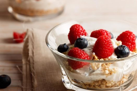 Raspberries, blueberries, cereals and yogurt in a glass bowl on sackcloth and wooden slats. Healthy breakfast for a healthy life. Horizontal image.