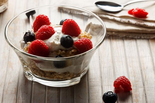 Raspberries, blueberries, cereals and yogurt in a glass bowl on wooden slats. Healthy breakfast for a healthy life. Horizontal image.
