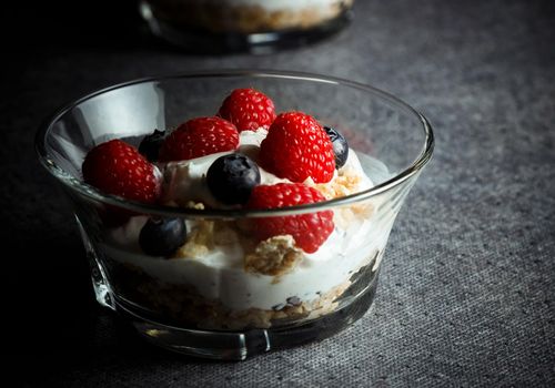 Raspberries, blueberries, cereals and yogurt in a glass bowl on a gray surface. Healthy breakfast for a healthy life. Horizontal image.