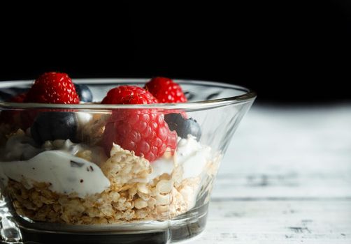 Raspberries, blueberries, cereals and yogurt in a glass bowl on wooden slats. Healthy breakfast for a healthy life. Horizontal image.