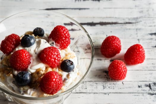 Raspberries, blueberries, cereals and yogurt in a glass bowl on wooden slats. Healthy breakfast for a healthy life. Horizontal image.