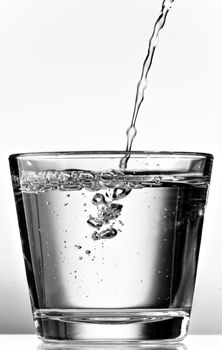 Pouring water into a glass cup on white background. Black and white.