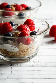 Raspberries, blueberries, cereals and yogurt in a glass bowl on wooden slats. Healthy breakfast for a healthy life. Vertical image.