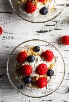 Raspberries, blueberries, cereals and yogurt in a glass bowl on wooden slats. Healthy breakfast for a healthy life. Vertical image view from above.