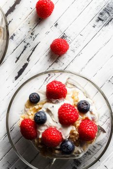 Raspberries, blueberries, cereals and yogurt in a glass bowl on wooden slats. Healthy breakfast for a healthy life. Vertical image view from above.