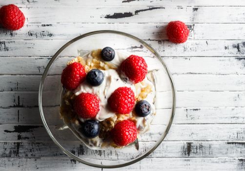 Raspberries, blueberries, cereals and yogurt in a glass bowl on wooden slats. Healthy breakfast for a healthy life. Horizontal image view from above.