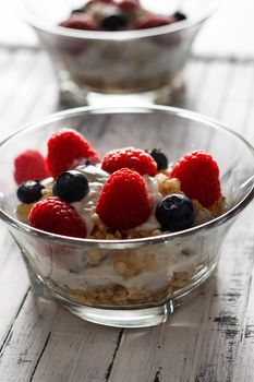 Raspberries, blueberries, cereals and yogurt in a glass bowl on wooden slats. Healthy breakfast for a healthy life. Vertical image.