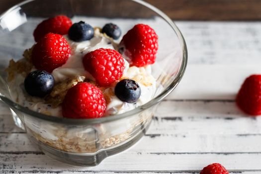 Raspberries, blueberries, cereals and yogurt in a glass bowl on wooden slats. Healthy breakfast for a healthy life. Horizontal image.