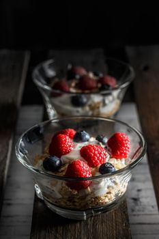 Raspberries, blueberries, cereals and yogurt in a glass bowl on old wooden boards. Healthy breakfast for a healthy life. Vertical image.