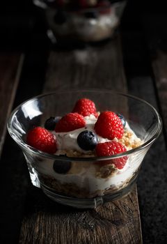 Raspberries, blueberries, cereals and yogurt in a glass bowl on old wooden boards. Healthy breakfast for a healthy life. Vertical image.