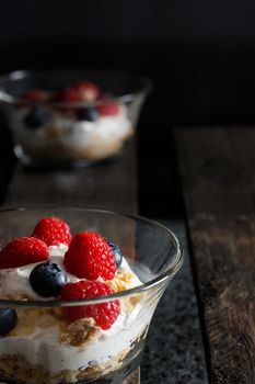 Raspberries, blueberries, cereals and yogurt in a glass bowl on old wooden boards. Healthy breakfast for a healthy life. Vertical image.