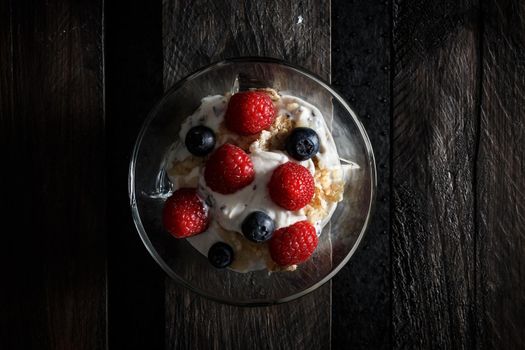 Raspberries, blueberries, cereals and yogurt in a glass bowl on old wooden boards. Healthy breakfast for a healthy life. Horizontal image view from above.