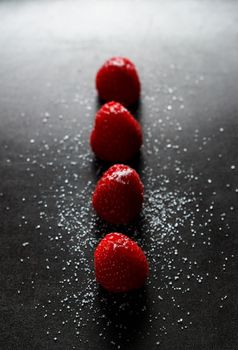 Red raspberries in a row with sugar on top on a black griddle. Backlighting. Vertical image.